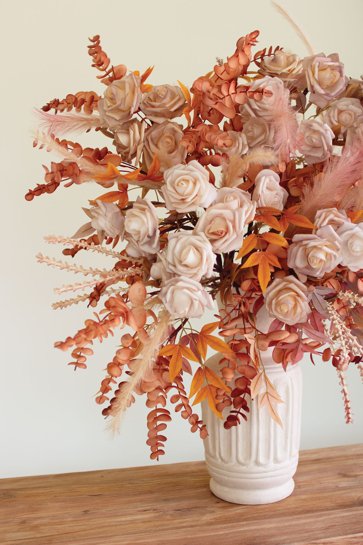 pale pink roses, pink feathers, and pink and orange leaves and eucalyptus in a white vase