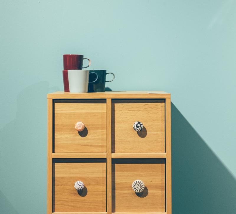 Dresser with four coffee cups on top in front of a teal wall
